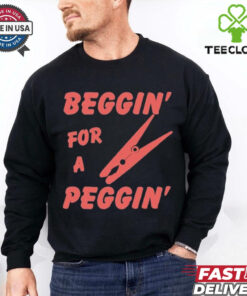 The **Beggin' For A Peggin' T-Shirt** features a playful and bold design, perfect for those who enjoy humor and a bit of cheeky fun. A great way to make a statement with a lighthearted and edgy style!