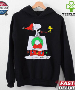Snoopy Woodstock Wreath Dog House Pullover Christmas Shirt featuring a festive design with Snoopy and Woodstock decorating a doghouse with a holiday wreath.