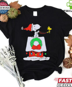 Snoopy Woodstock Wreath Dog House Pullover Christmas Shirt featuring a festive design with Snoopy and Woodstock decorating a doghouse with a holiday wreath.